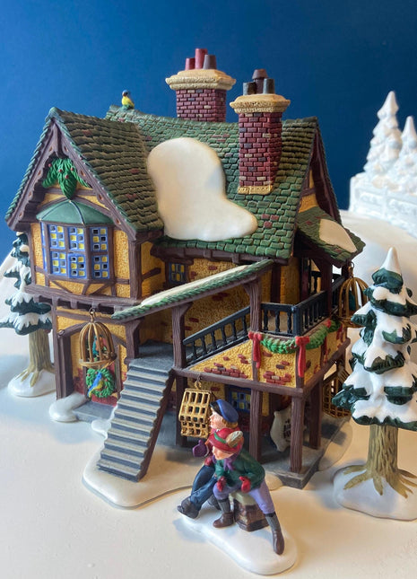Illuminated Porcelain Christmas Village "Wingham Lane Parrot Seller" House" by Dept 56. and Woman Holding Bird Cage, Dickens Village, 1999.
