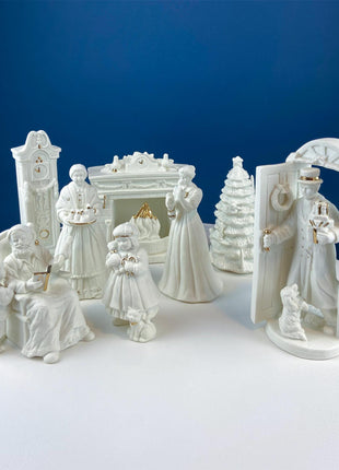 White Porcelain Figurines of Santa & His Family Celebrating Christmas in Front of Fireplace. Illuminated Fireplace and Tree. Mantel Display.