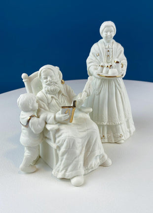 White Porcelain Figurines of Santa & His Family Celebrating Christmas in Front of Fireplace. Illuminated Fireplace and Tree. Mantel Display.